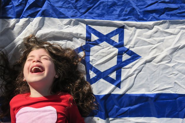 Child smiling next to Israeli flag