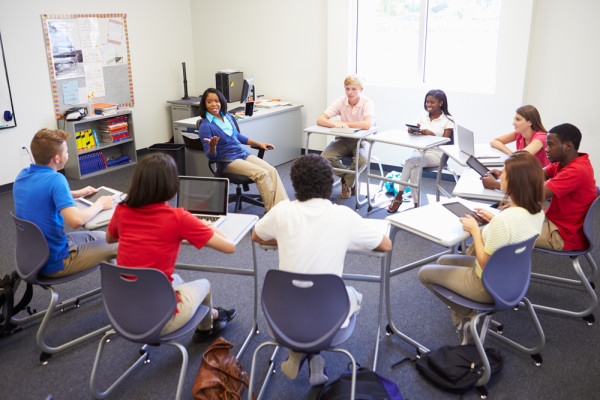 Students sitting in a circle of desks, talking to one another