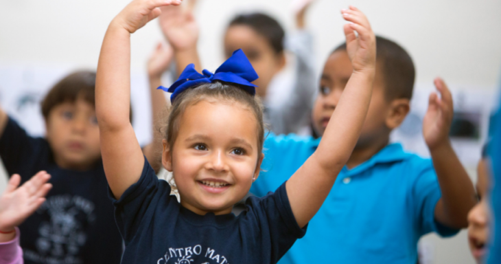 Smiling young child with hands raised in dancing position with other children