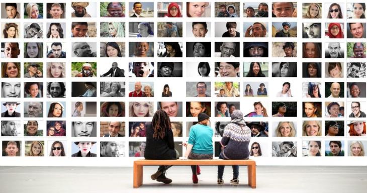 3 people sitting on bench in front of massive display of multi-cultural images of people