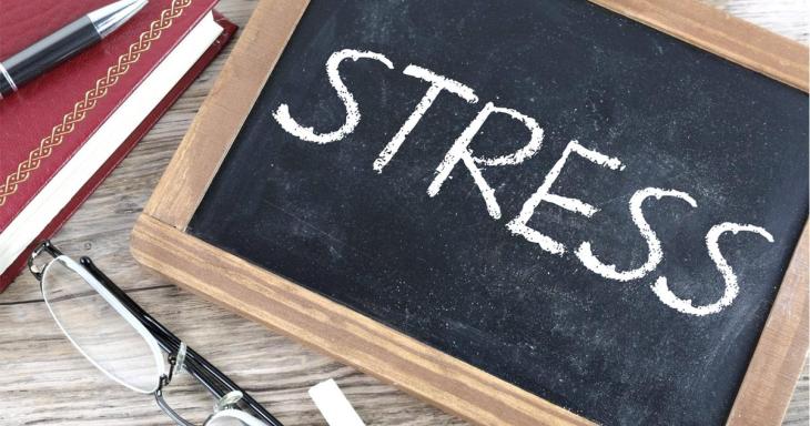 Stress written on chalk board in all caps, with a notebook, pencil, and reading glasses