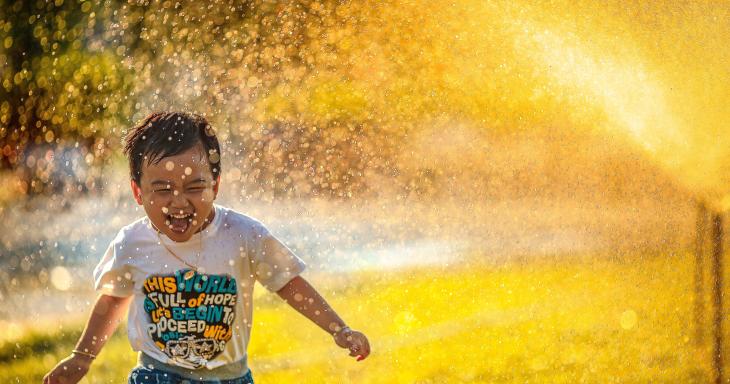 Smiling child running through sprinklers