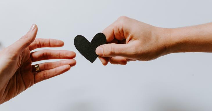 A hand handing a paper heart to another