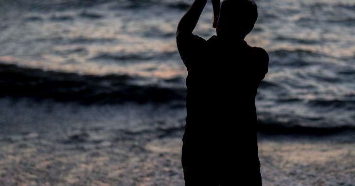 A person blowing the Shofar on a beach at sunset