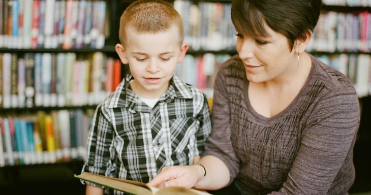 A teacher sits with a boy and shows him a picture book