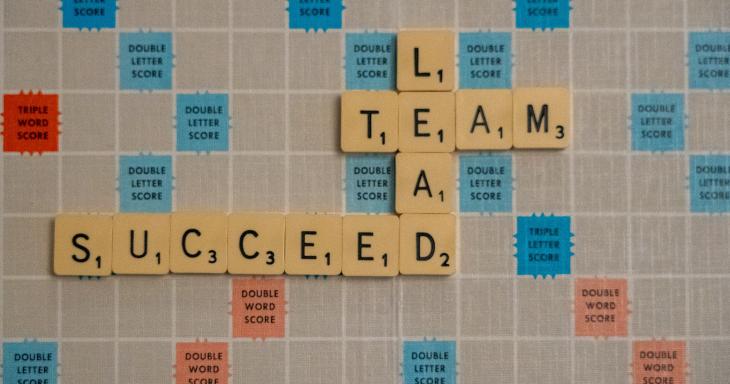 A Scrabble board with tiles that spell out Team, Succeed, and Lead