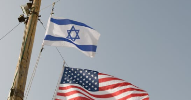 An Israeli flag attached to a pole waves above an American flag