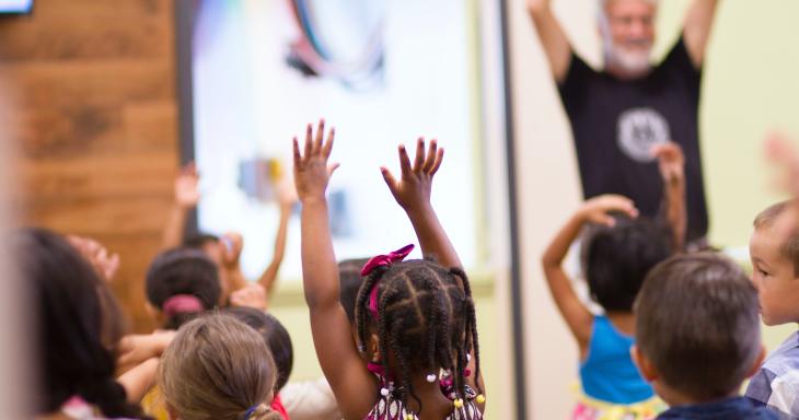 children in a classroom holding hands up