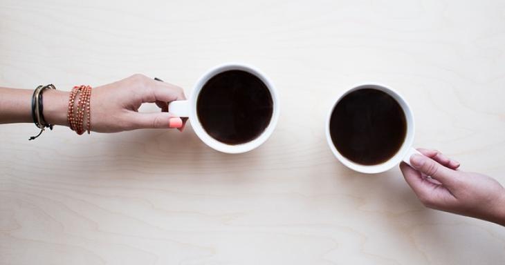 two hands, each holding a coffee mug, reach out to each other