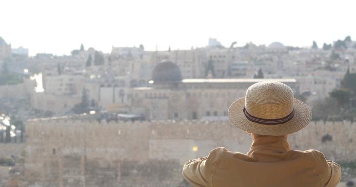 A man sits, back to the camera, with the Old City and al-Aqsa mosque visible in the background. 