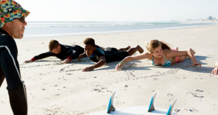 An instructor on a beach teaching three teenagers how to surf