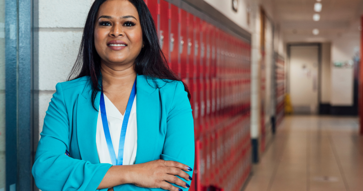 A female teacher in a blue jacket stands in a hallway with lockers in the background
