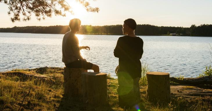 Two people sitting by a lake and talking. 