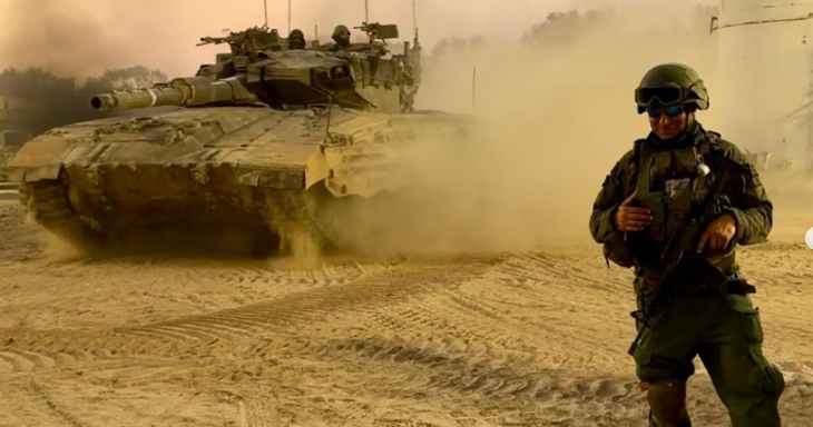 Tuvia Book stands in full army uniform with a tank behind him