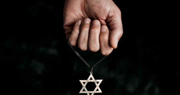 A hand holds a dangling Star of David necklace against a black background