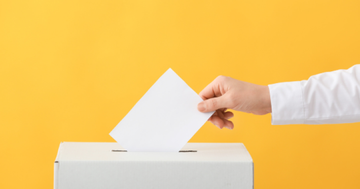 a hand puts a ballot in a box with a yellow background