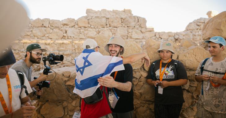 teenage boys hugging at top of Masada with Israeli flag