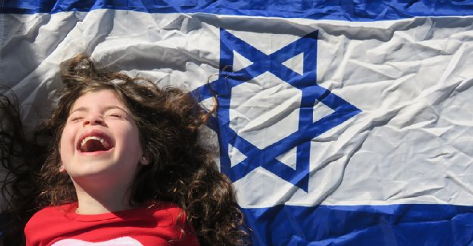 Child smiling next to Israeli flag