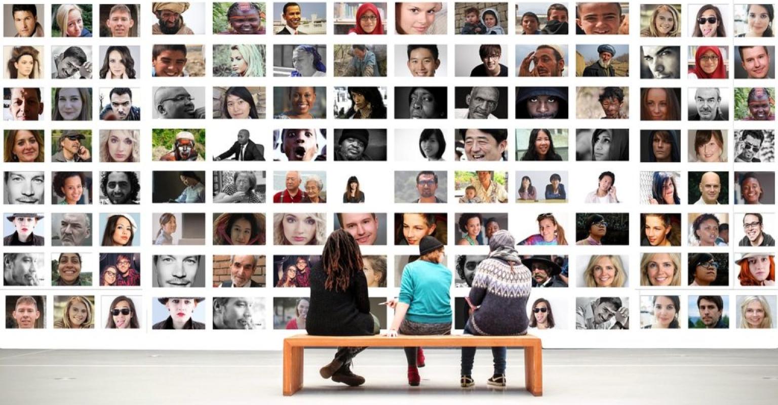 3 people sitting on bench in front of massive display of multi-cultural images of people