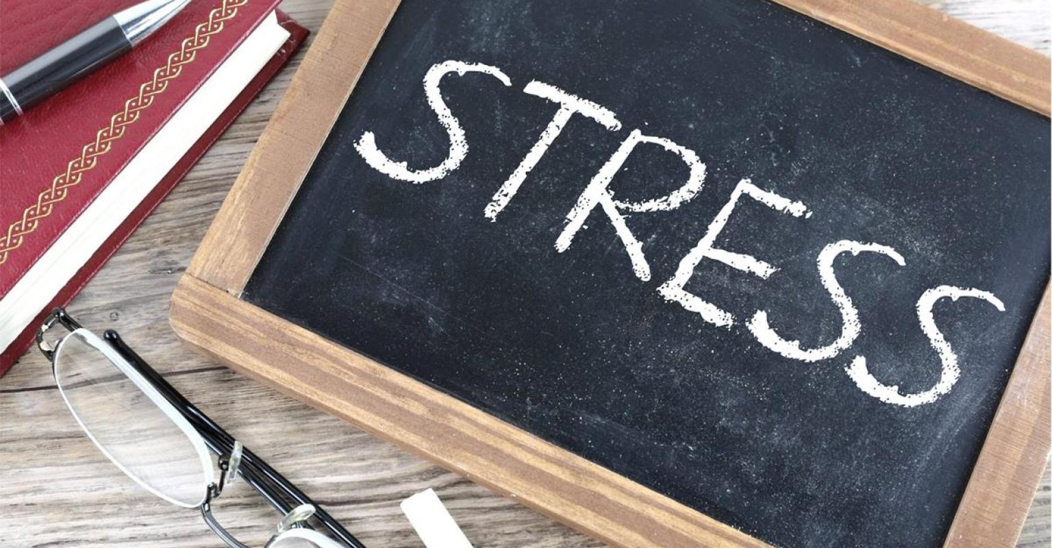 Stress written on chalk board in all caps, with a notebook, pencil, and reading glasses