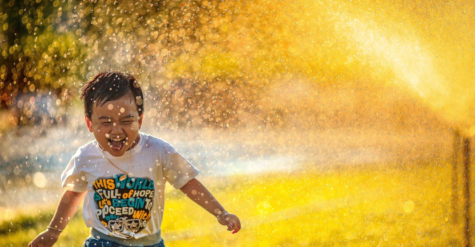 Smiling child running through sprinklers