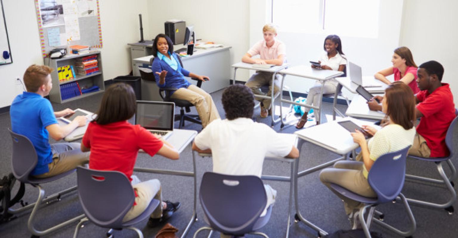 Students sitting in a circle of desks, talking to each other