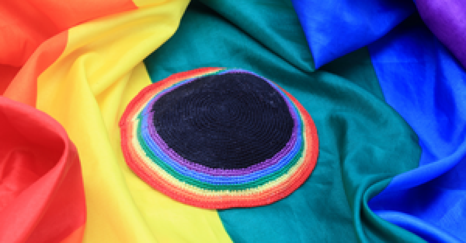 A rainbow yarmulke sits on top of a pride flag