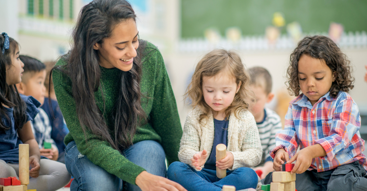 A teacher crouching down with her young students playing