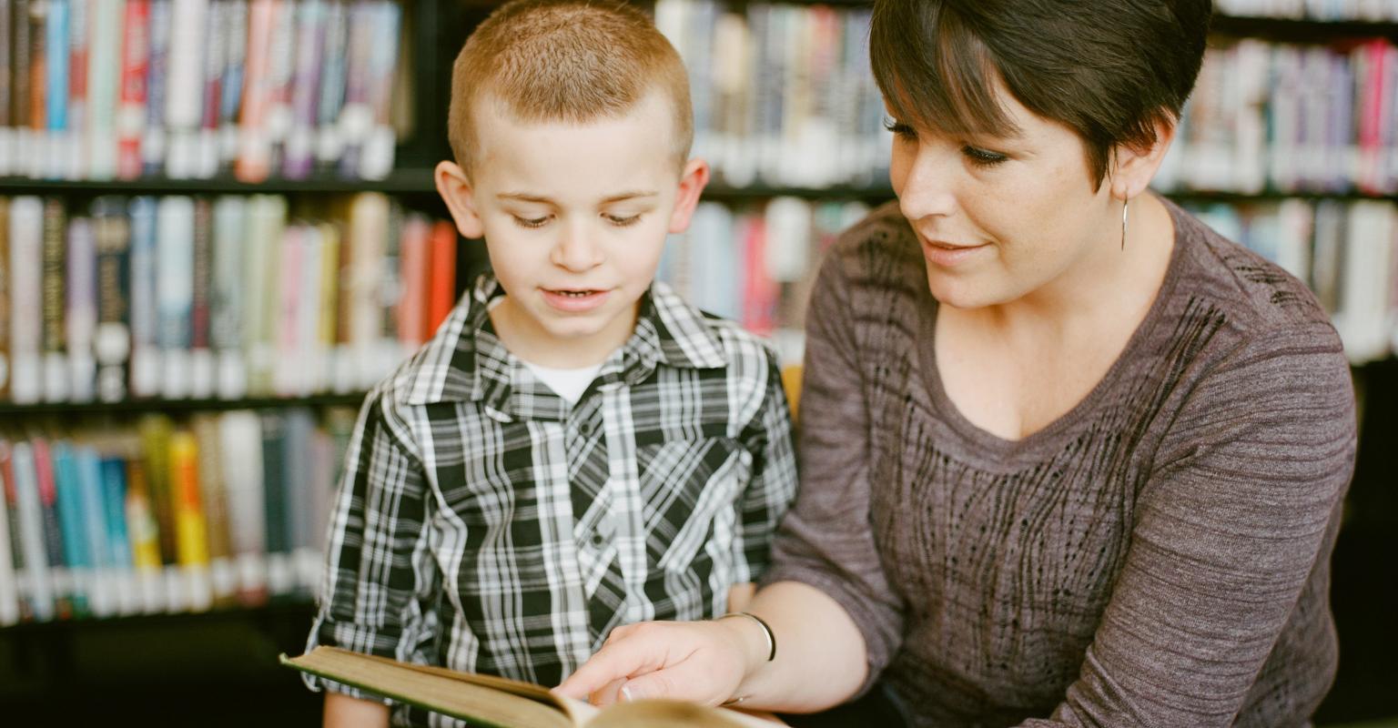 A teacher looks at a book with a young boy