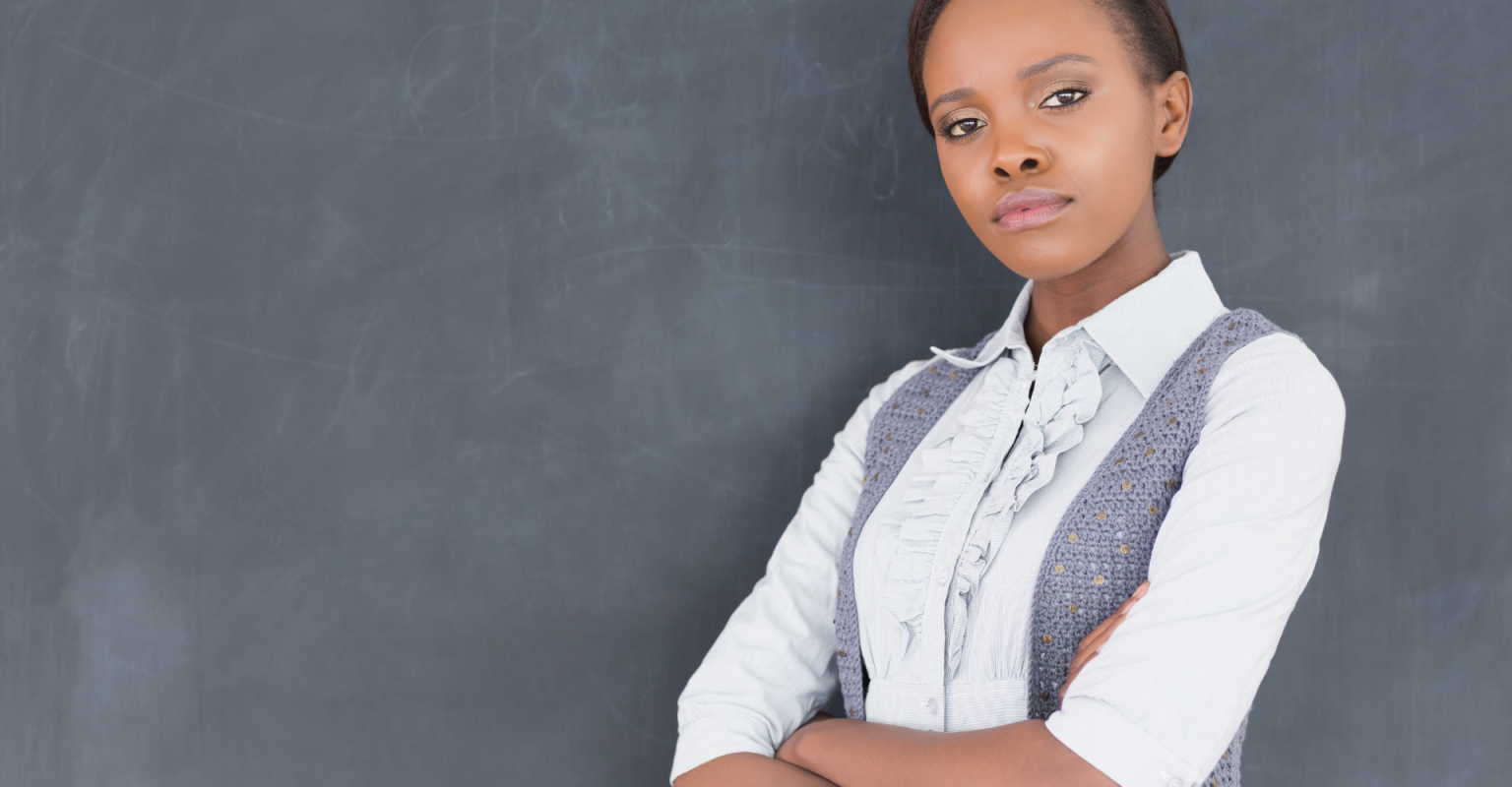 A woman looking serious with her arms crossed in front of a chalkboard