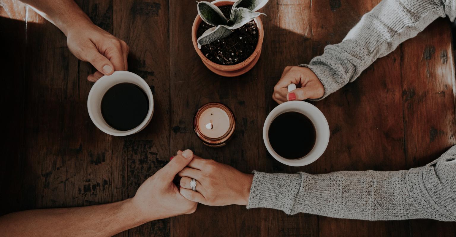 Two people holding hands over coffee. 