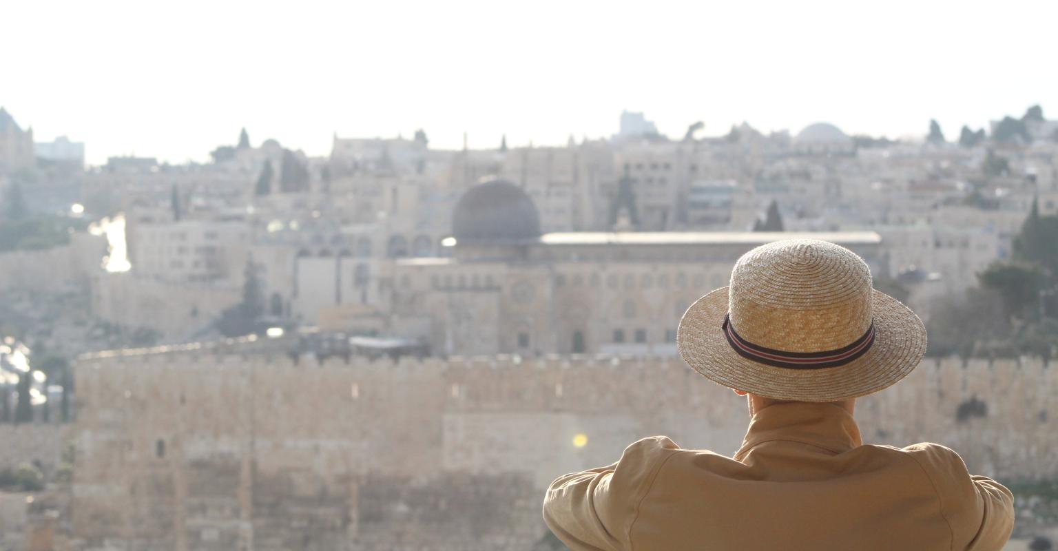 A man sits, back to the camera, with the Old City and al-Aqsa mosque visible in the background.