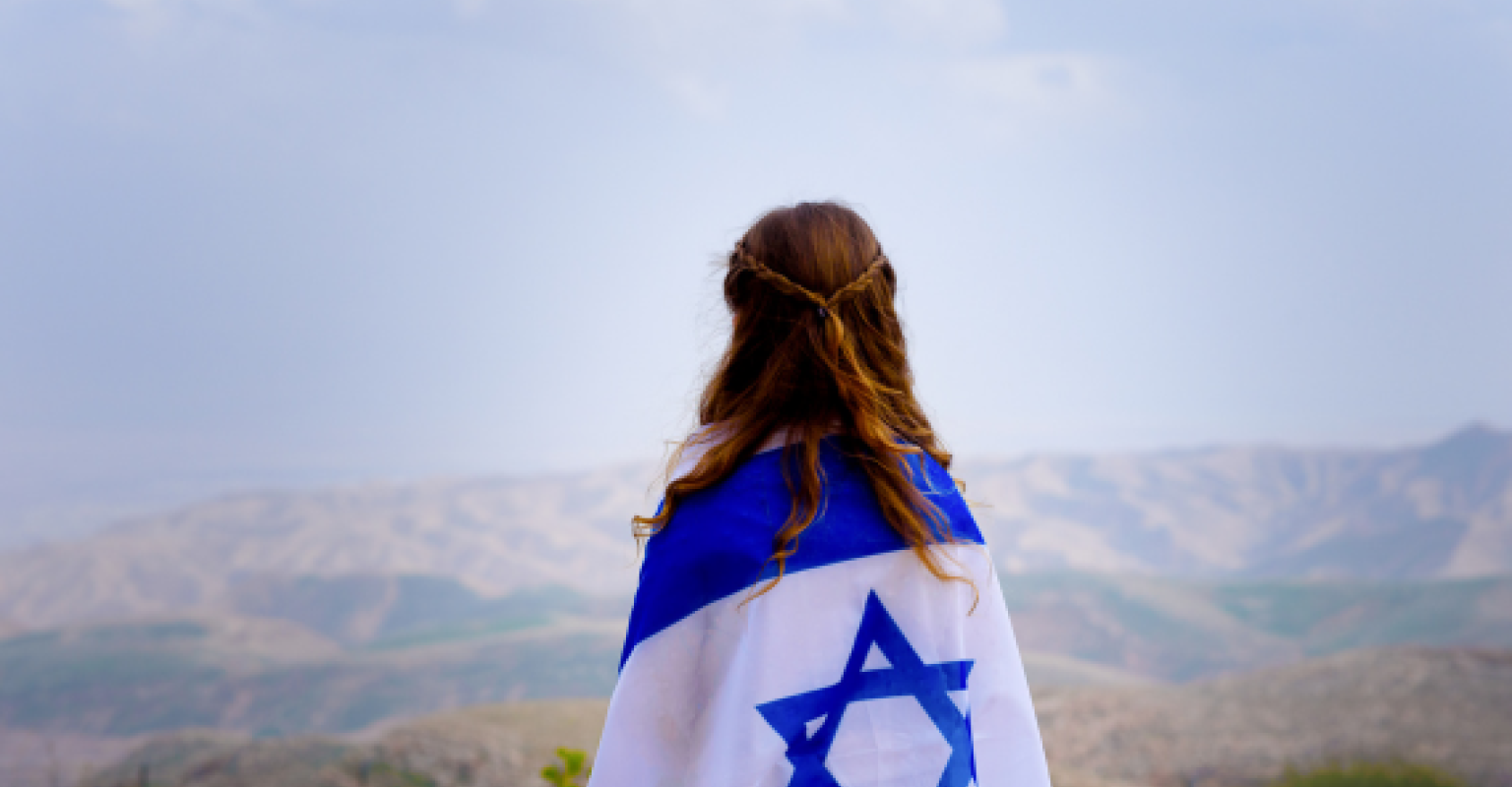 Girl with Israeli flag wrapped around her faces mountains