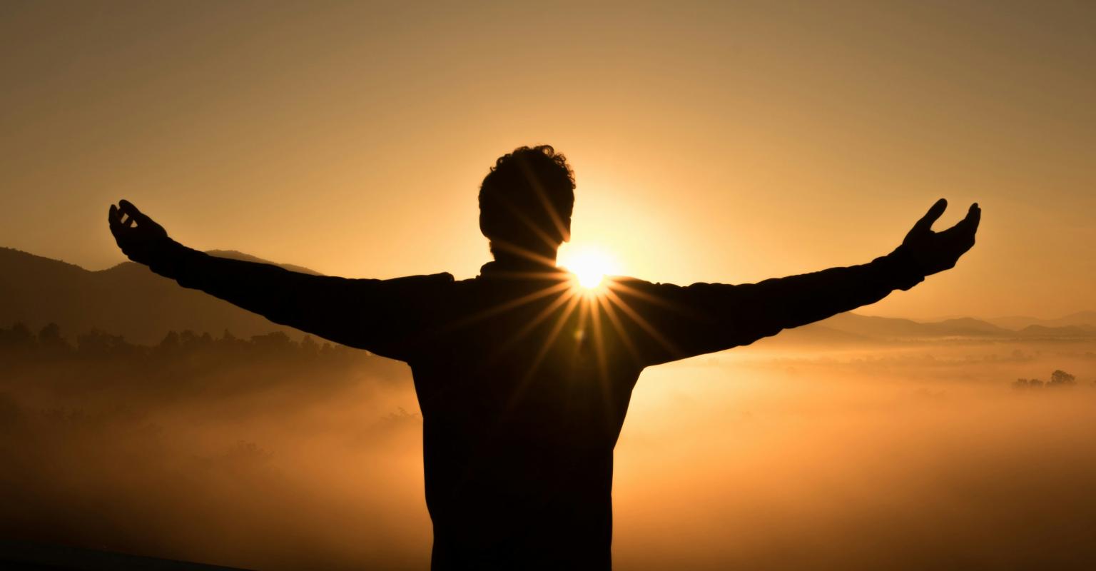 Person raising hands in sunset