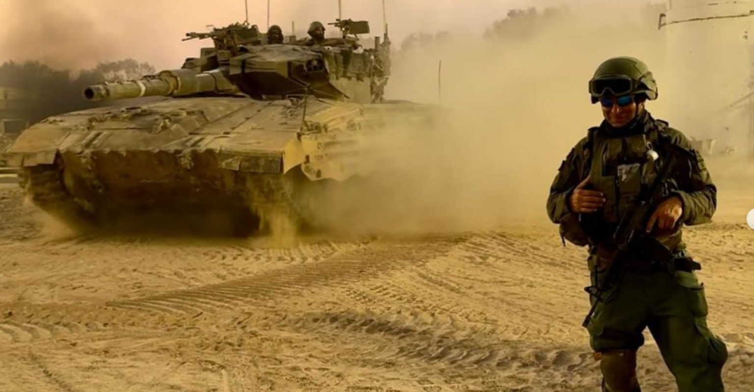 Tuvia Book stands in full army uniform with a tank behind him