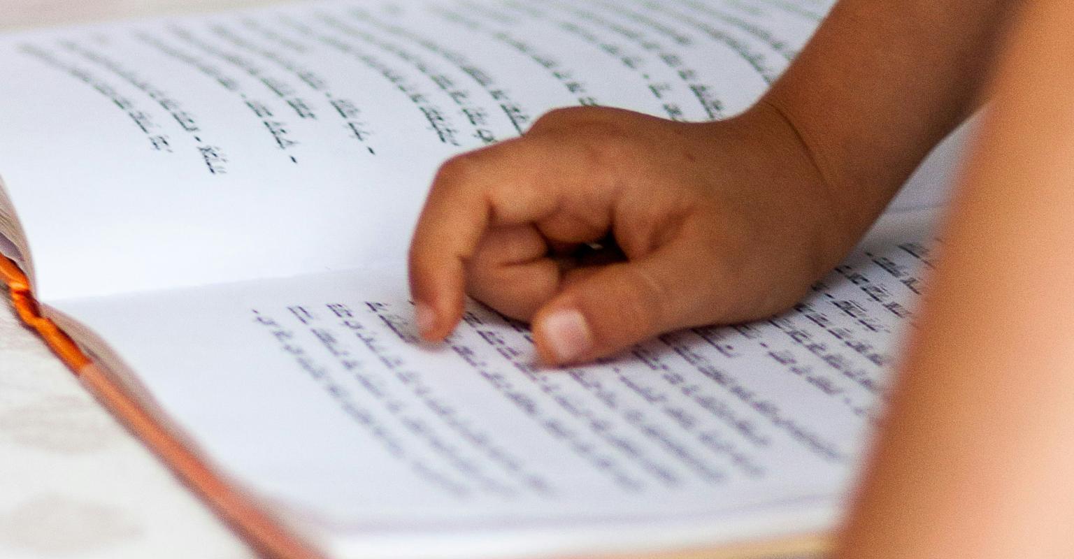 A child's hands studying text from a Hebrew book. 