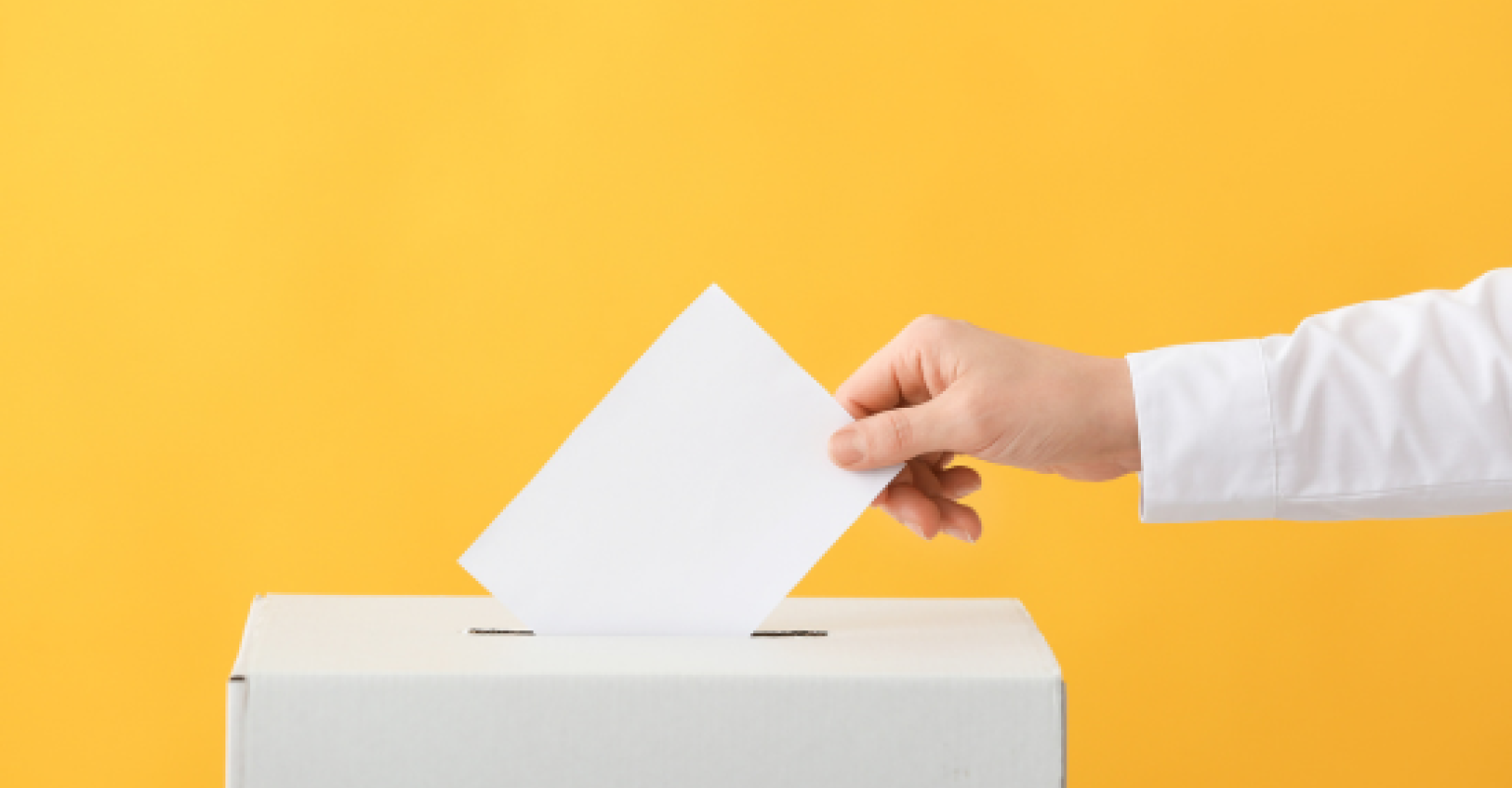 a hand puts a ballot in a box with a yellow background