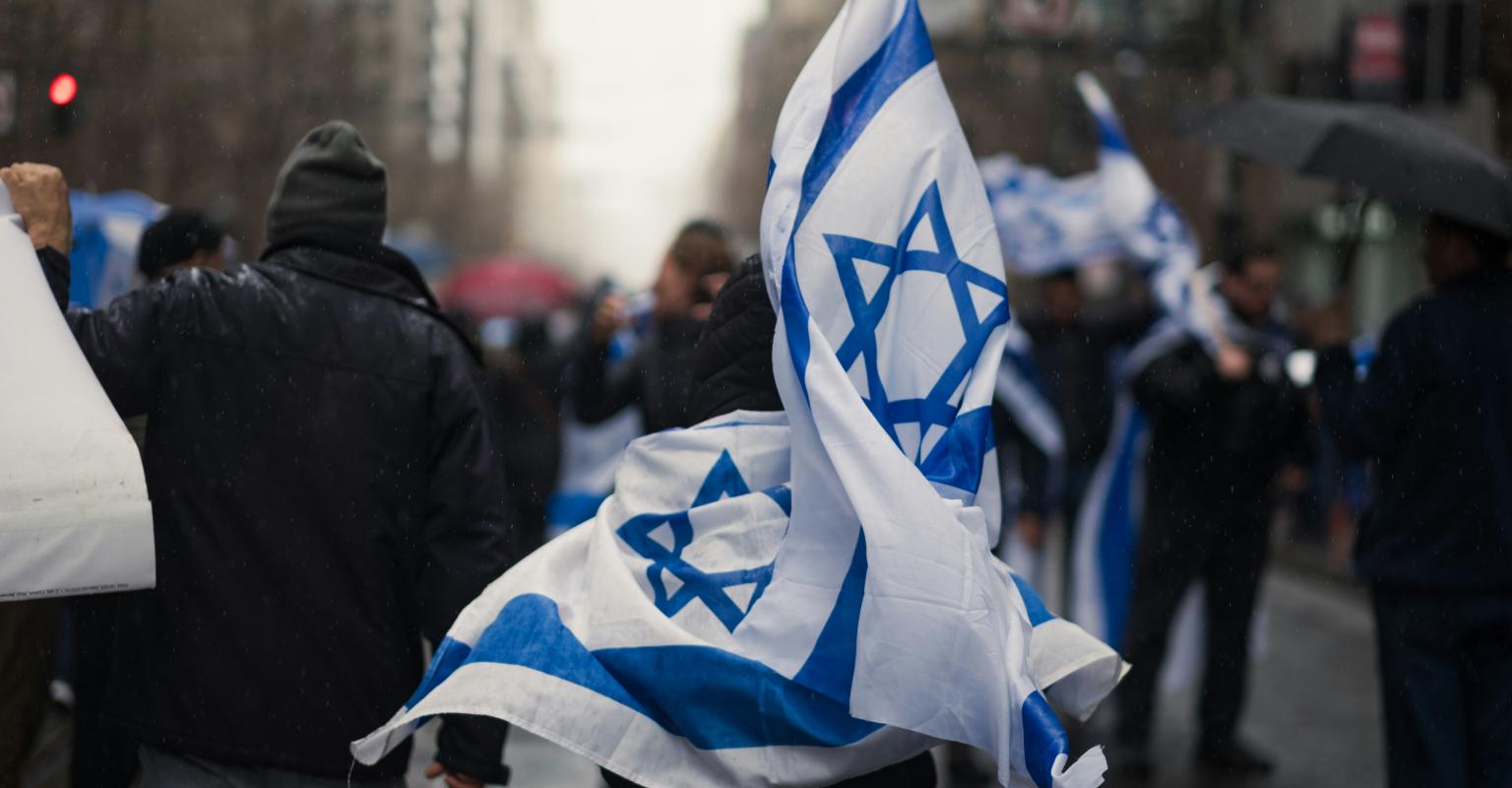 A marcher at a rally holding two Israeli flags. 