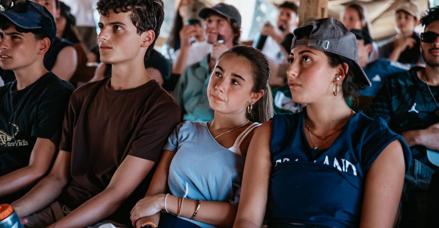 Group of teens sitting in rows, watching and listening
