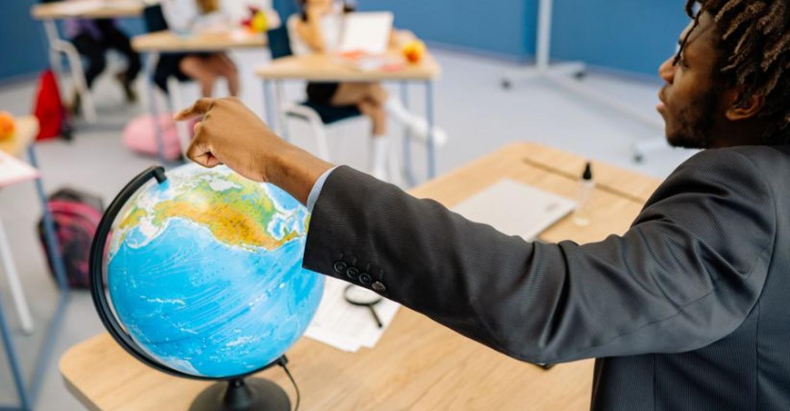 a teacher at front of classroom points to globe