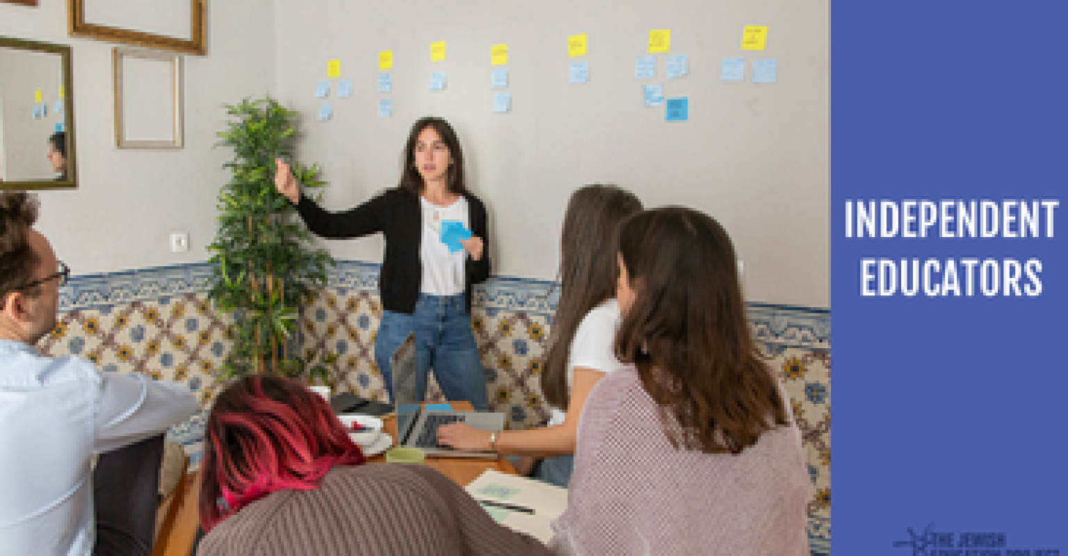 "Independent Educators" banner. Facilitator standing and speaking with sticky notes behind them. Participants sit at a table. 