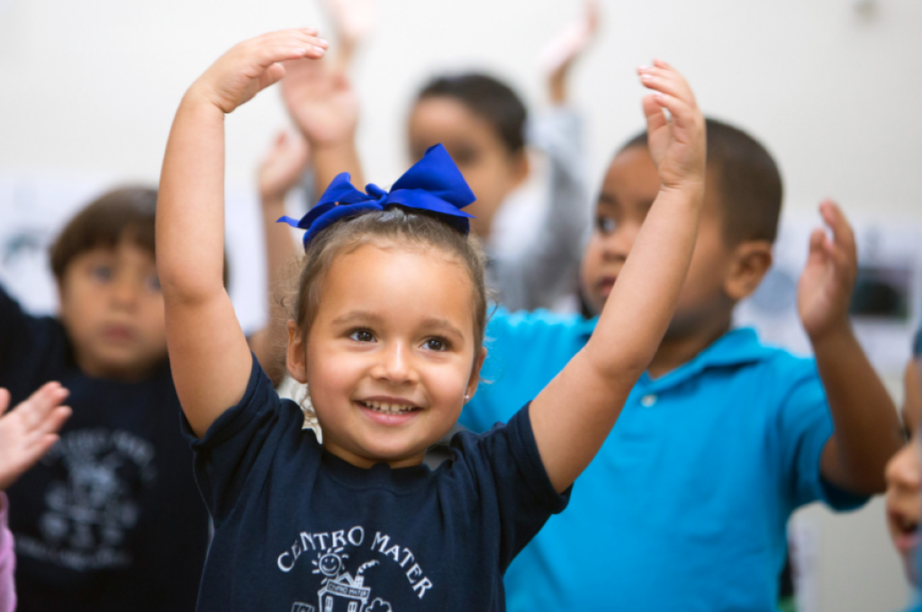 Smiling young child with hands raised in dancing position with other children