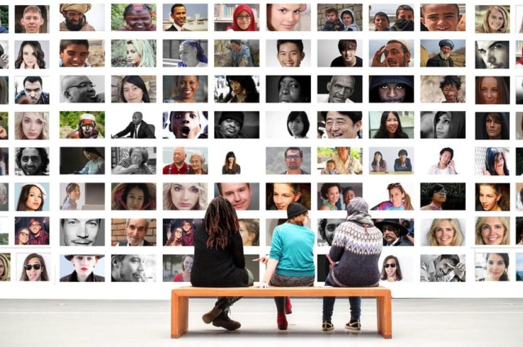 3 people sitting on bench in front of massive display of multi-cultural images of people