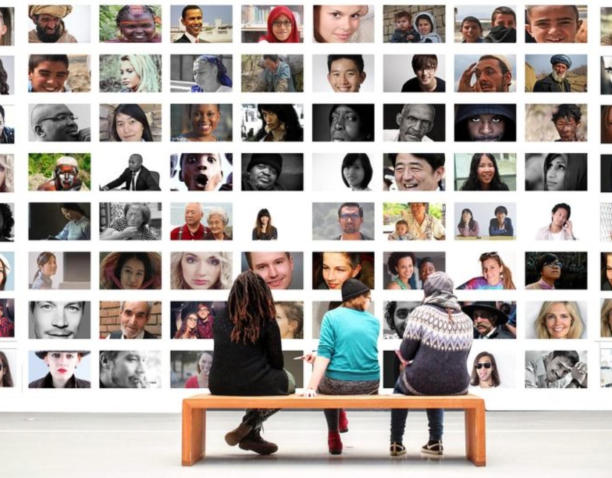 3 people sitting on bench in front of massive display of multi-cultural images of people