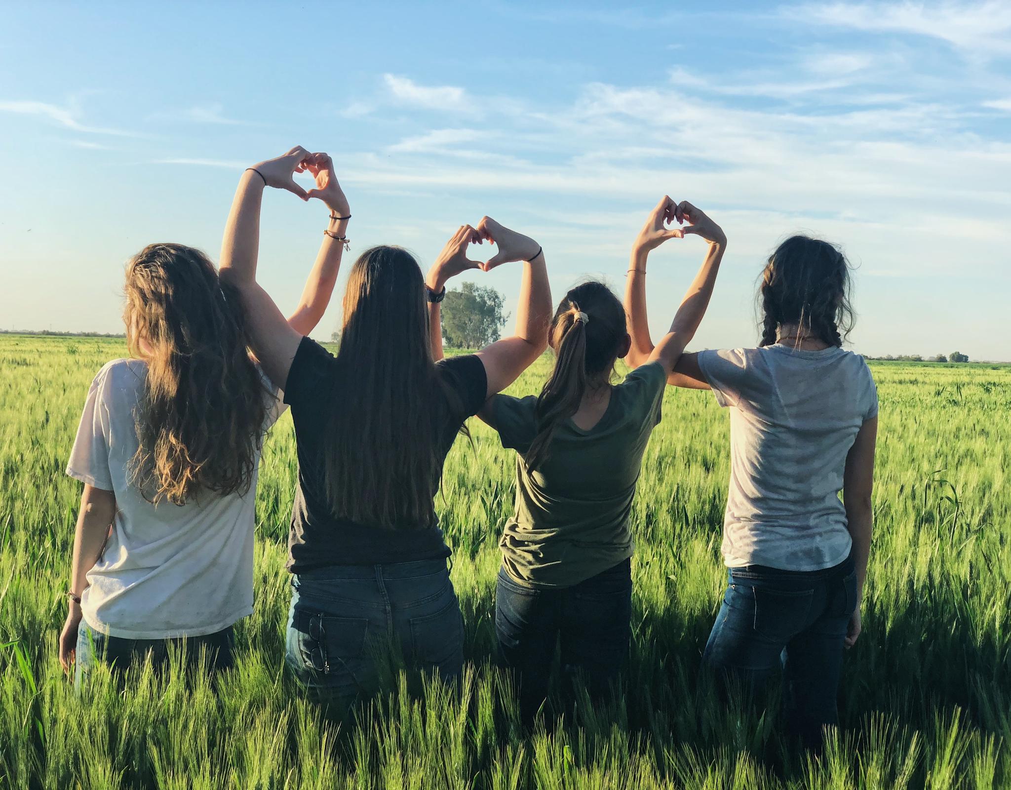 Four children sit in a field with their back to the camera, making hearts with their hands together. 