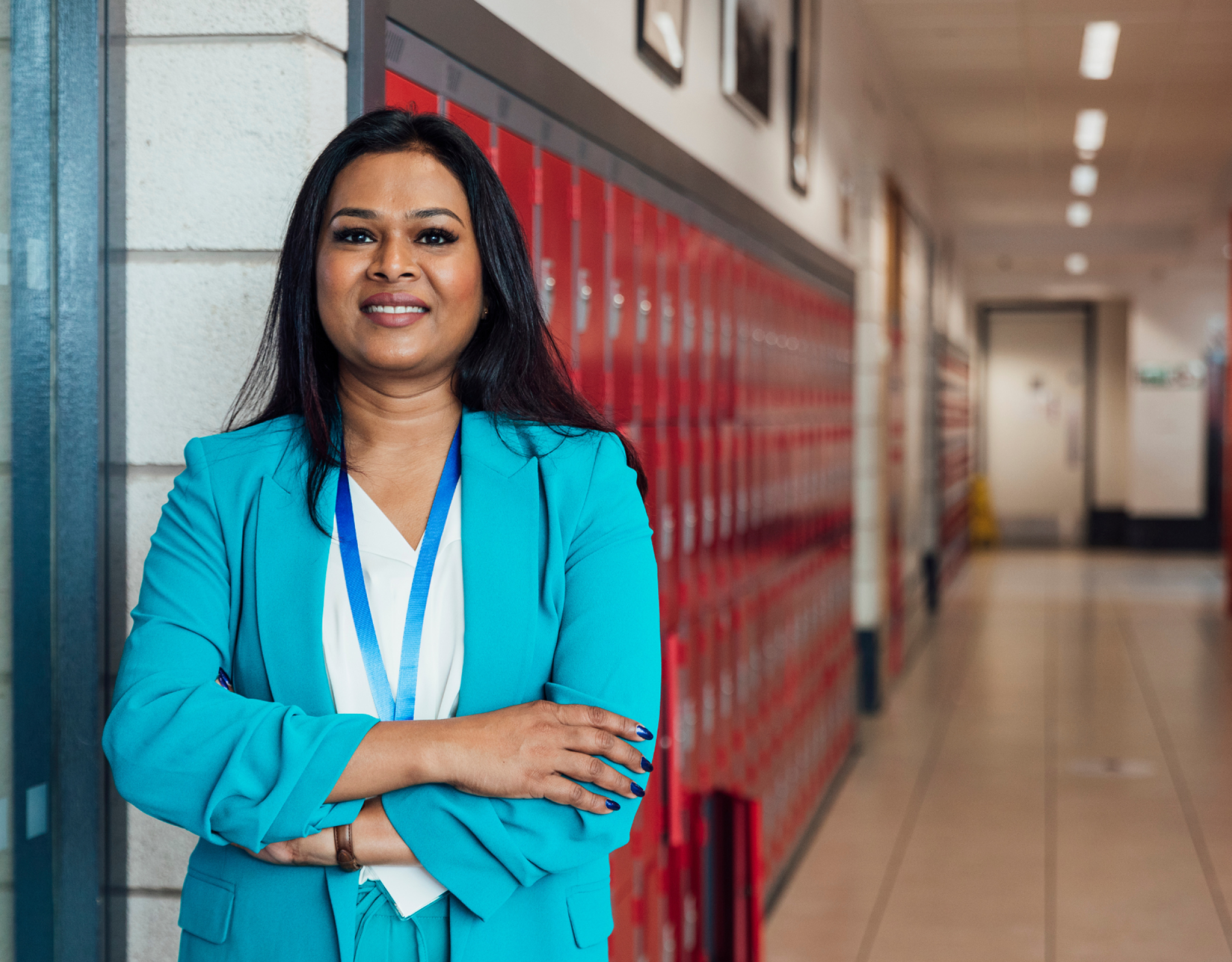 A female teacher in a blue jacket stands in a hallway with lockers in the background