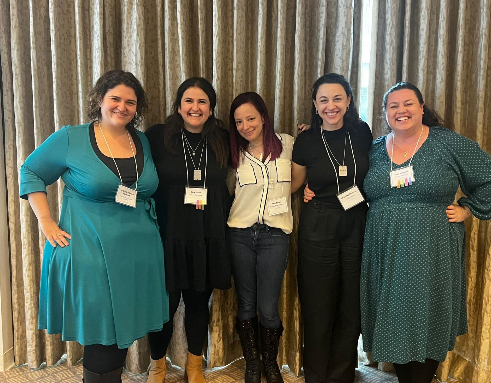 a group of women pose with arms around each other, each with nametags around their necks