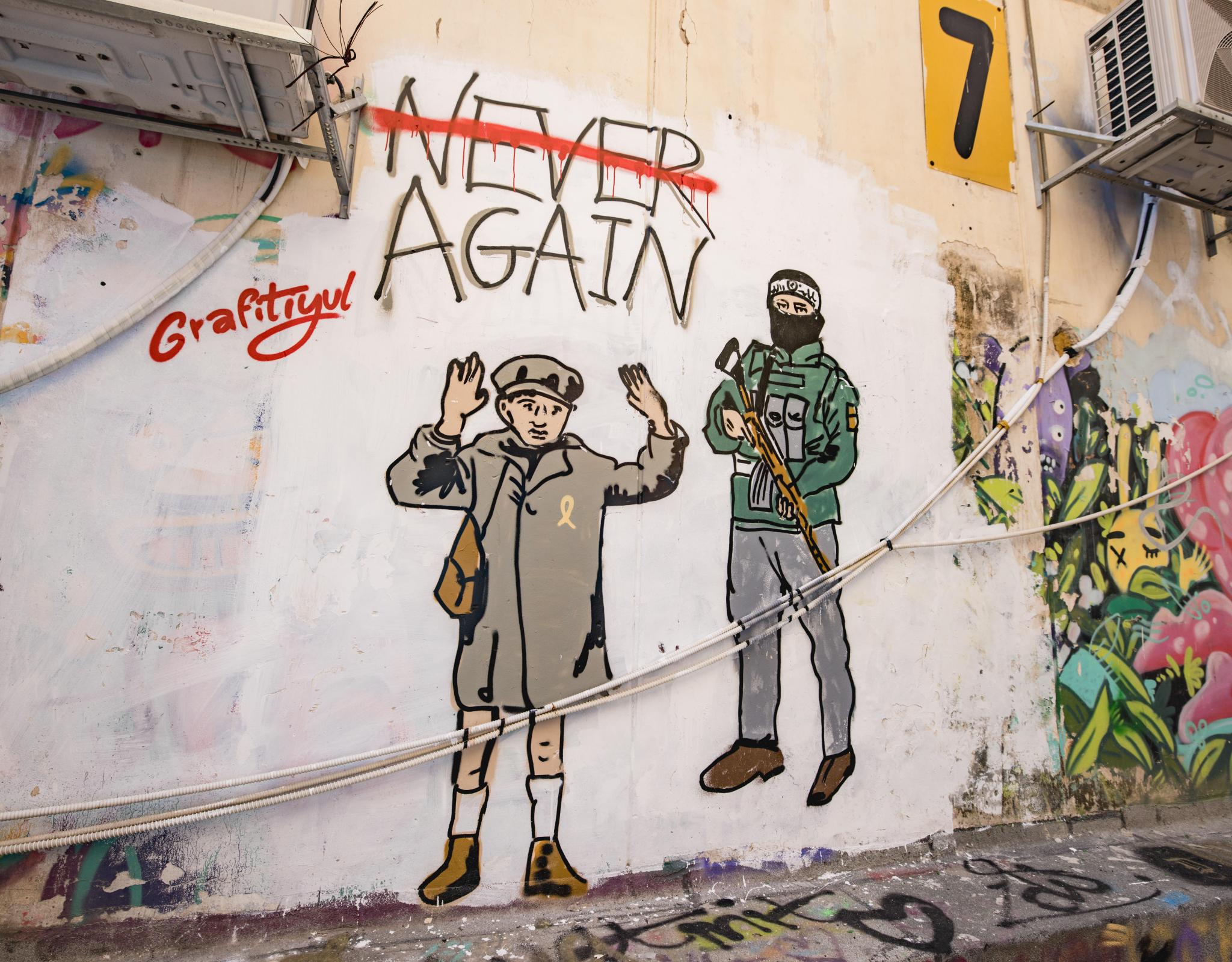 graffiti of hamas militant holding gun next to boy from the holocaust with his hands up, words say "never again" but never is crossed out