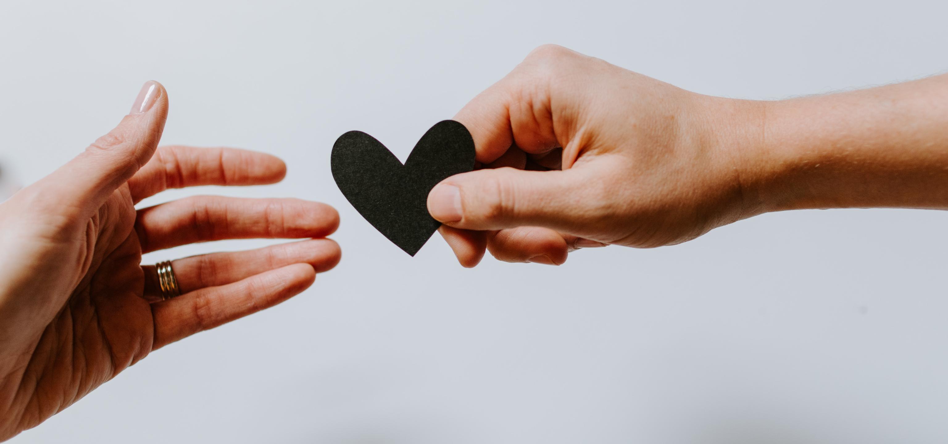 A hand handing a paper heart to another