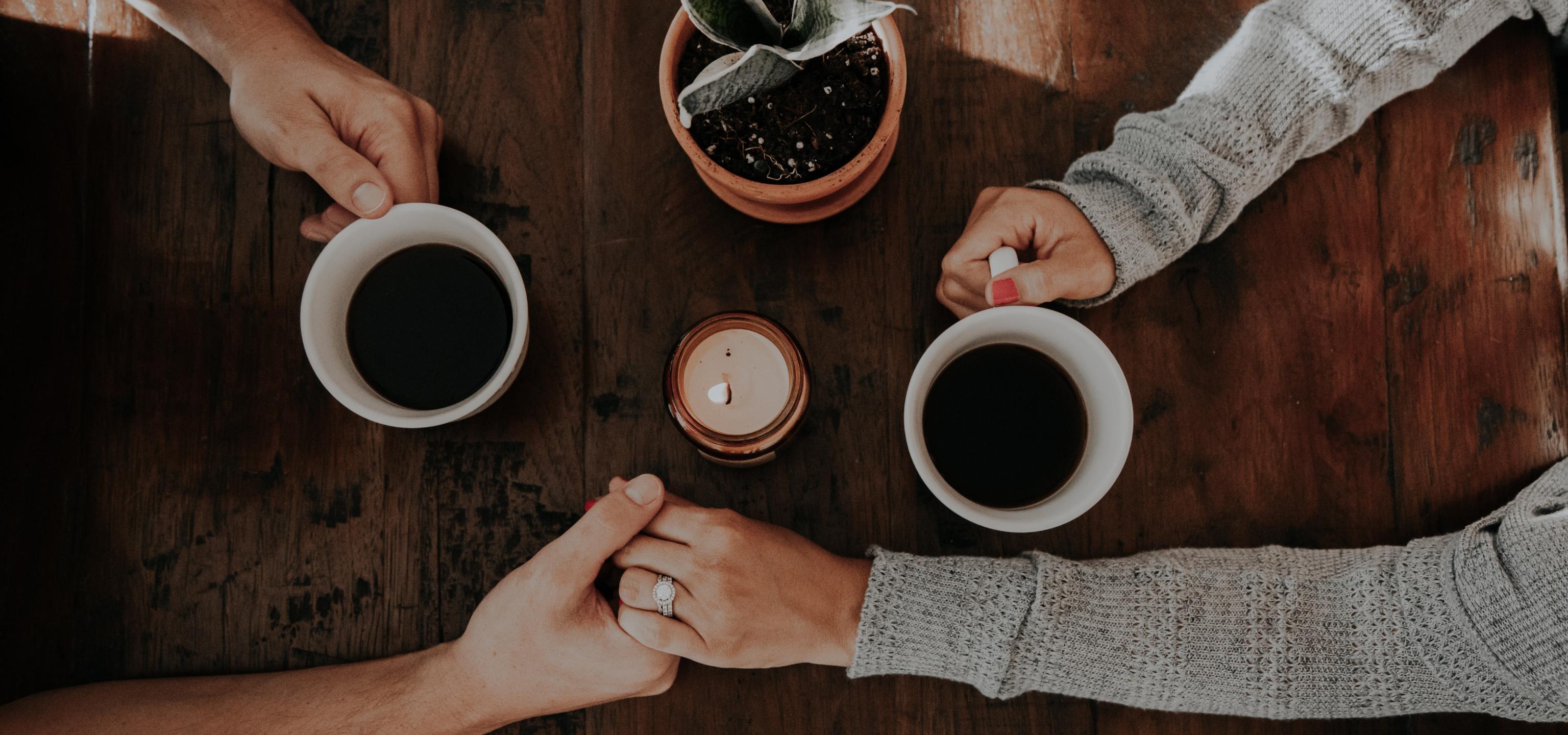 Two people holding hands over coffee. 
